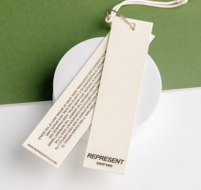 Neutral coloured swing tags with printed brand and care information, styled on a clean green backdrop.