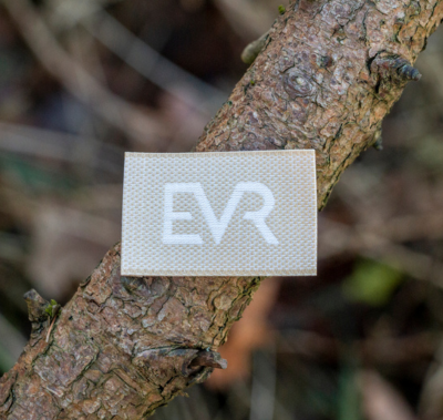 EVR woven brand label photographed on a tree branch, highlighting sustainable branding in a natural environment.