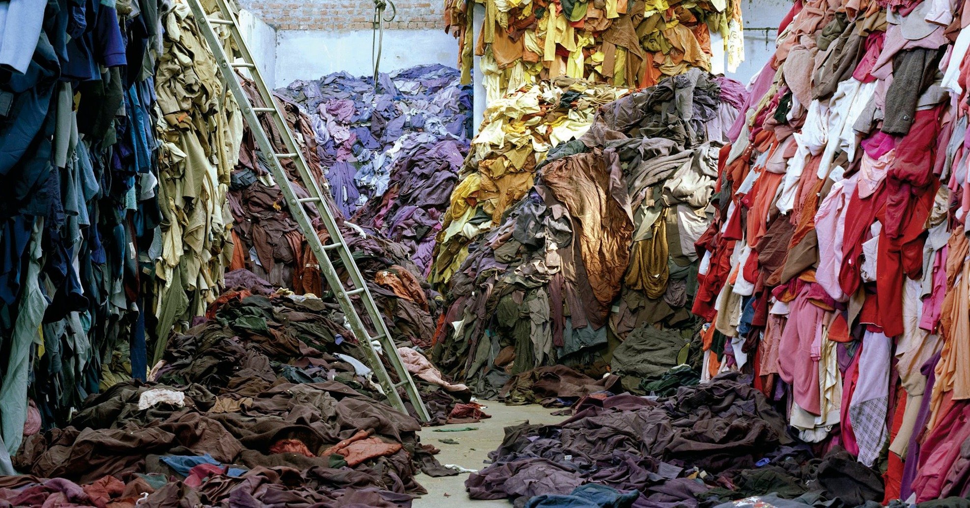 Photograph of clothing waste, organized by color and piled high.